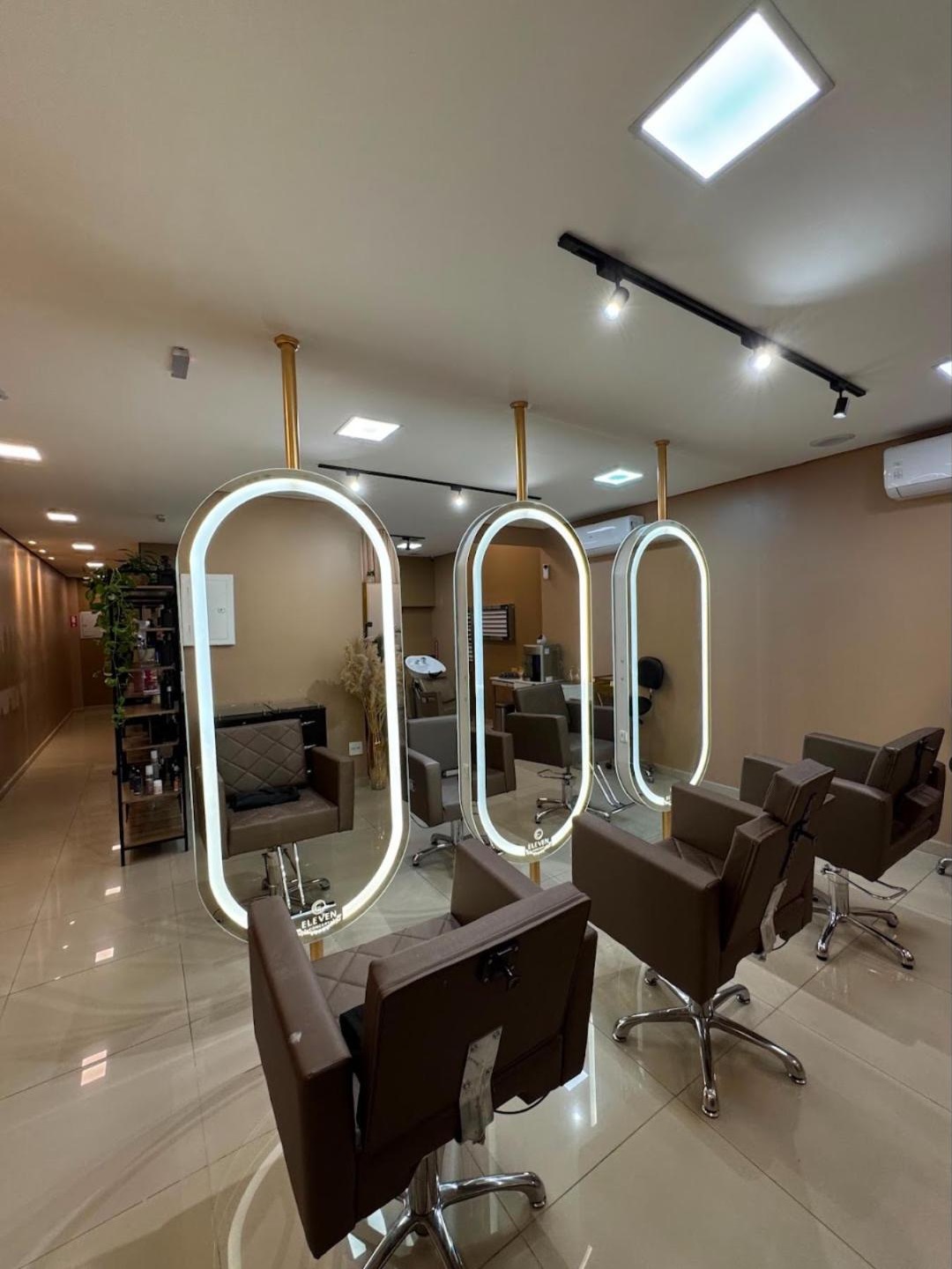 Salão do Eleven Concept com três espelhos ovais iluminados e poltronas de couro marrom